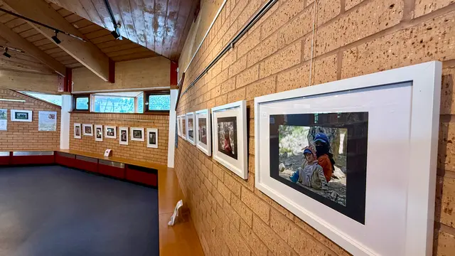 A row of framed photographs along a brick gallery wall beneath sloping windows.