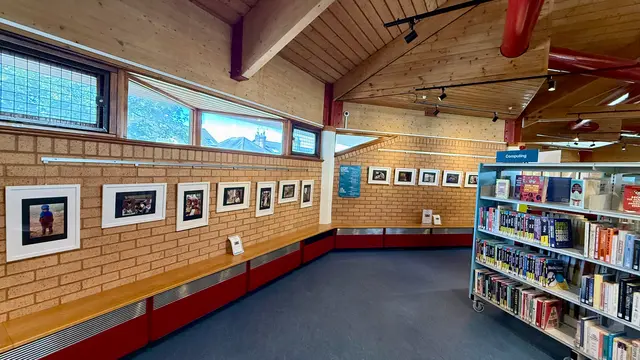 Wide view of the library gallery, with framed photographs on brick walls and bookshelves to the right.