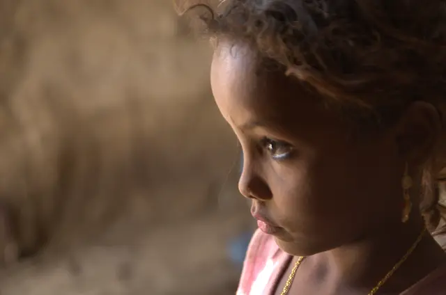 Close profile of a young girl with curly hair, looking down in soft light.