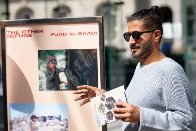 A man in sunglasses holds photographs beside a panel headed ‘The Other Refuge — Fuad Al-Gaadi’.