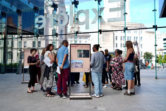 Visitors stand around a freestanding photography panel beneath the atrium’s glass roof.